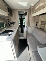 Efficient RV rental interior: compact kitchen with sink, stovetop, and microwave, plus comfy dinette and rear bath area.