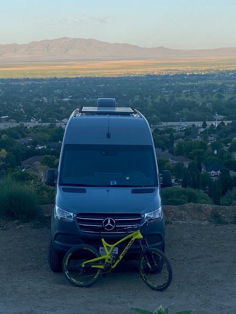 RV rental adventure: A Mercedes Sprinter camper van with a mountain bike, parked at a scenic overlook above a valley.