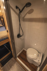 Modern RV rental wet bath featuring a shower, toilet, white subway tile, and a slatted wood floor.