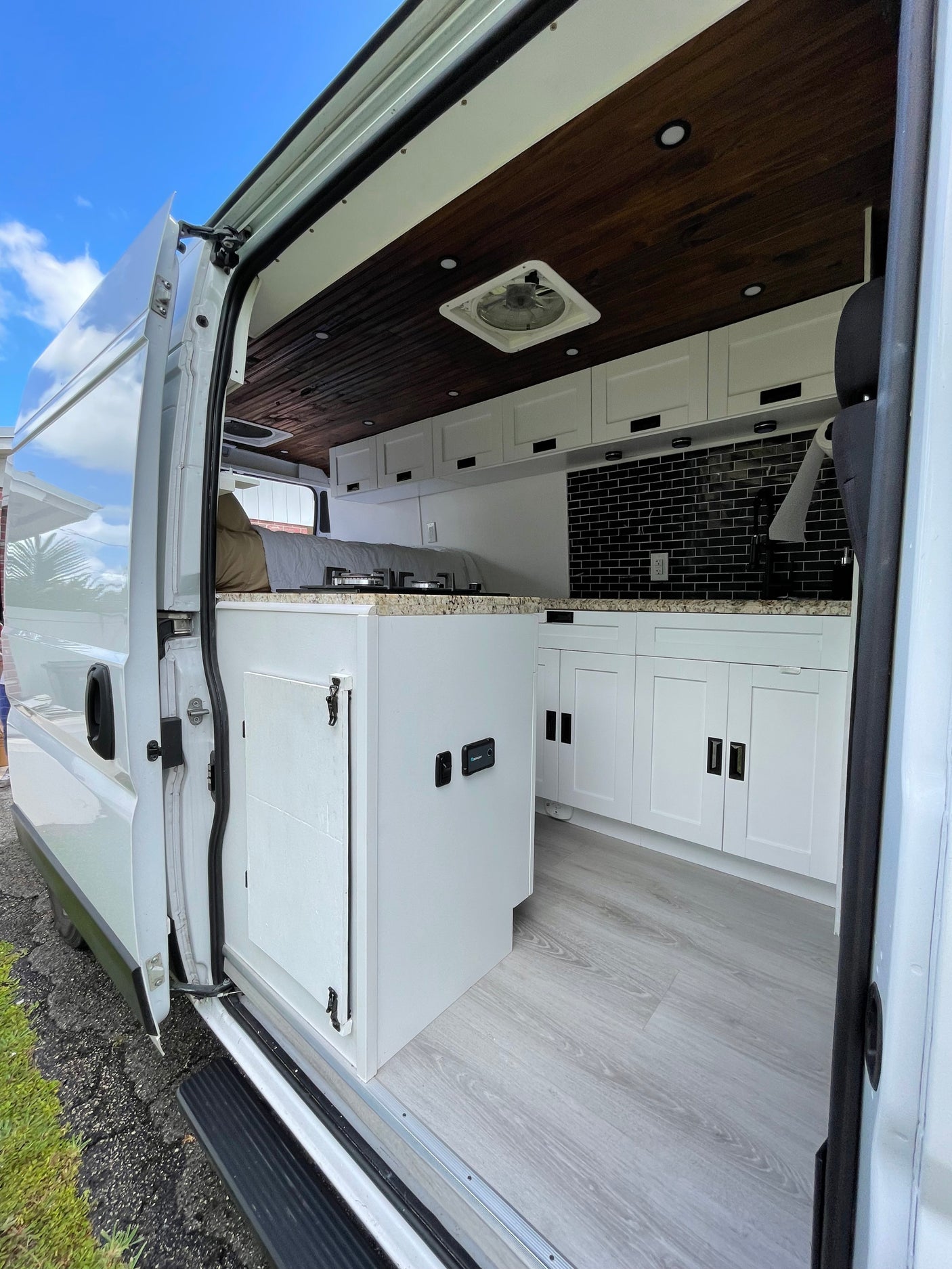 Spacious RV rental interior showcasing a dark wood ceiling, white kitchen with black backsplash, and light wood-look flooring.