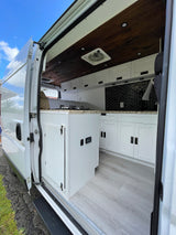 Spacious RV rental interior showcasing a dark wood ceiling, white kitchen with black backsplash, and light wood-look flooring.