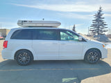 White minivan with rooftop tent available for RV rental, parked outdoors. Ideal for exploring as a compact camper van.