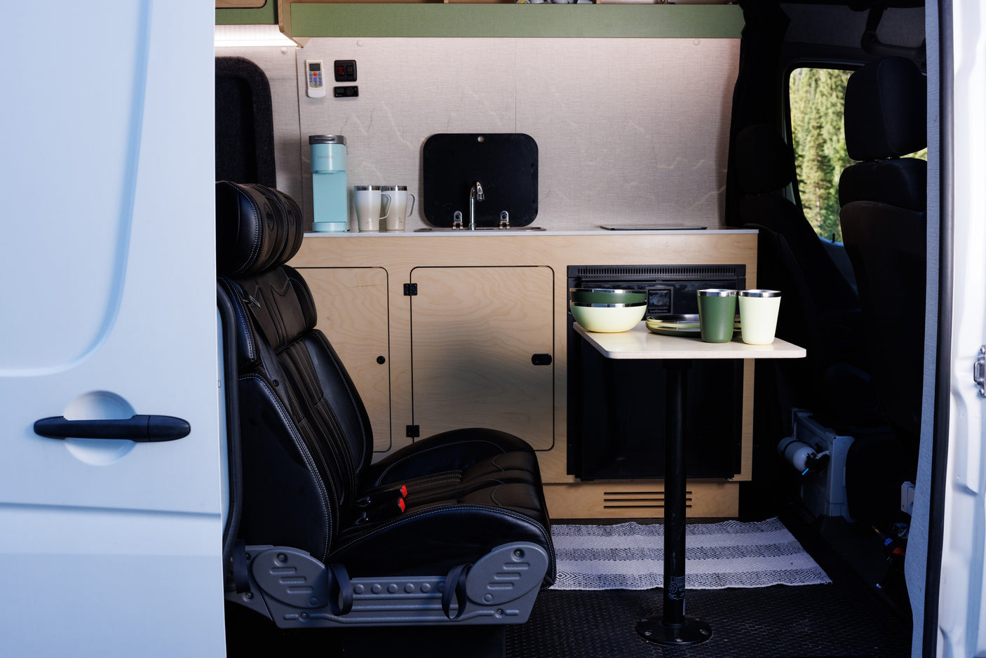 Bright RV rental interior: compact kitchen with sink, coffee maker, dining table, and passenger seat, ready for adventure.
