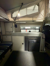 Cozy RV rental interior with pop-top, galley, Dometic fridge, and bench seating. Ready for your next road trip.
