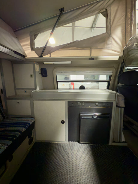Cozy RV rental interior with pop-top, galley, Dometic fridge, and bench seating. Ready for your next road trip.