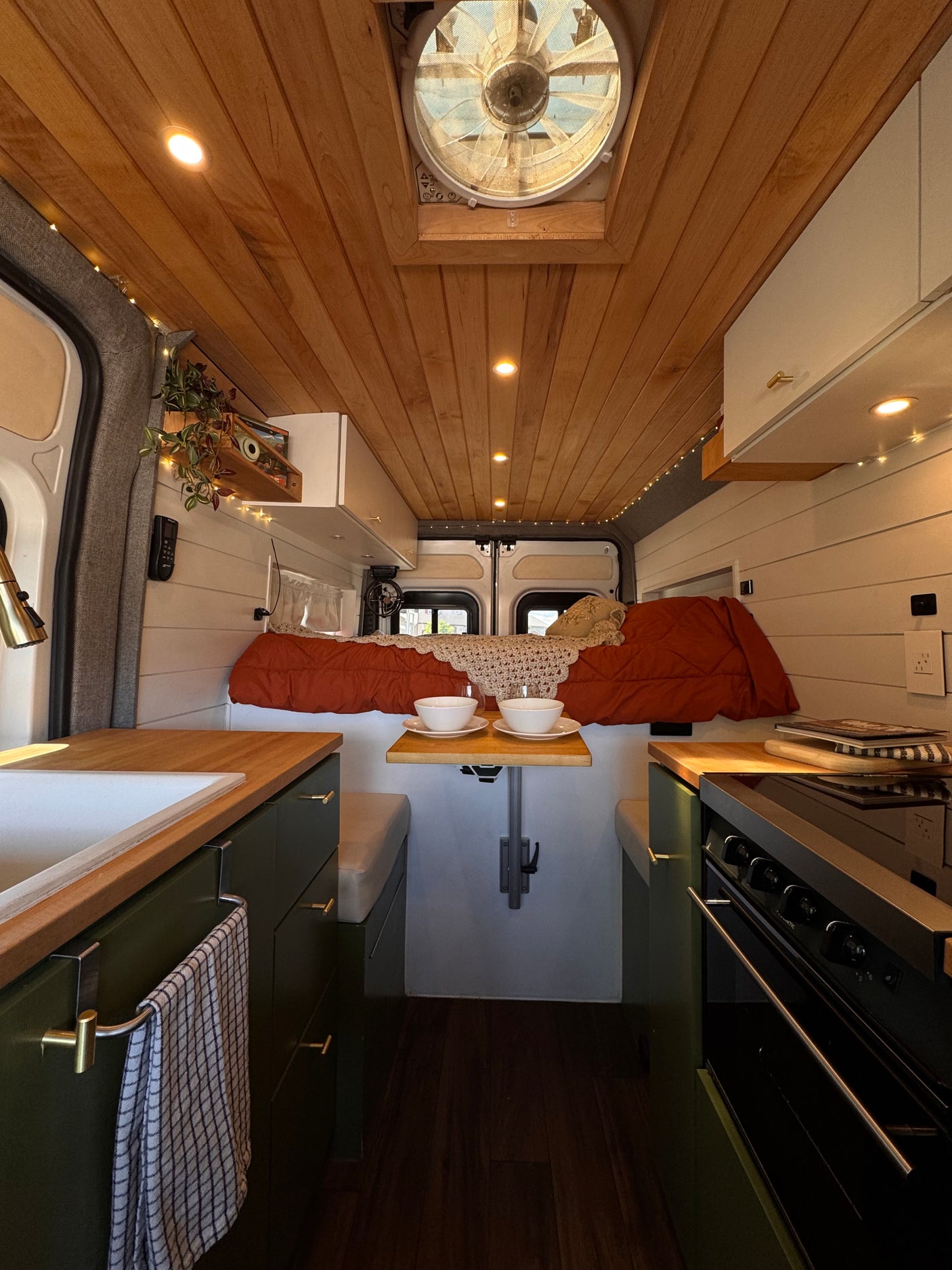 Stylish rv rental interior: wooden ceiling, compact kitchen, dining table, and cozy bed. Perfect for van life adventures.