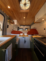 Stylish rv rental interior: wooden ceiling, compact kitchen, dining table, and cozy bed. Perfect for van life adventures.