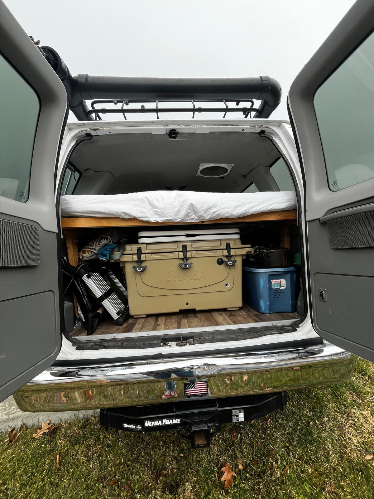 RV rental van's organized back: bed, cooler, camping gear, roof rack, & hitch visible. Ready for adventure. — photo 10