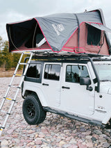 White Jeep Wrangler, iKamper rooftop tent deployed, ladder to riverbed. A unique RV rental for overlanding.