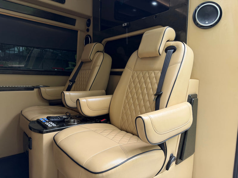 Luxury RV rental interior with tan leather seats, diamond stitching, armrests, cup holders, and remotes. — photo 9