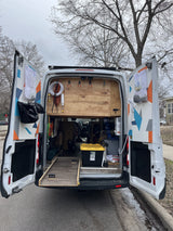 Open rear doors of an RV rental van reveal a custom-built interior with organized gear, an outdoor shower, and pull-out storage.