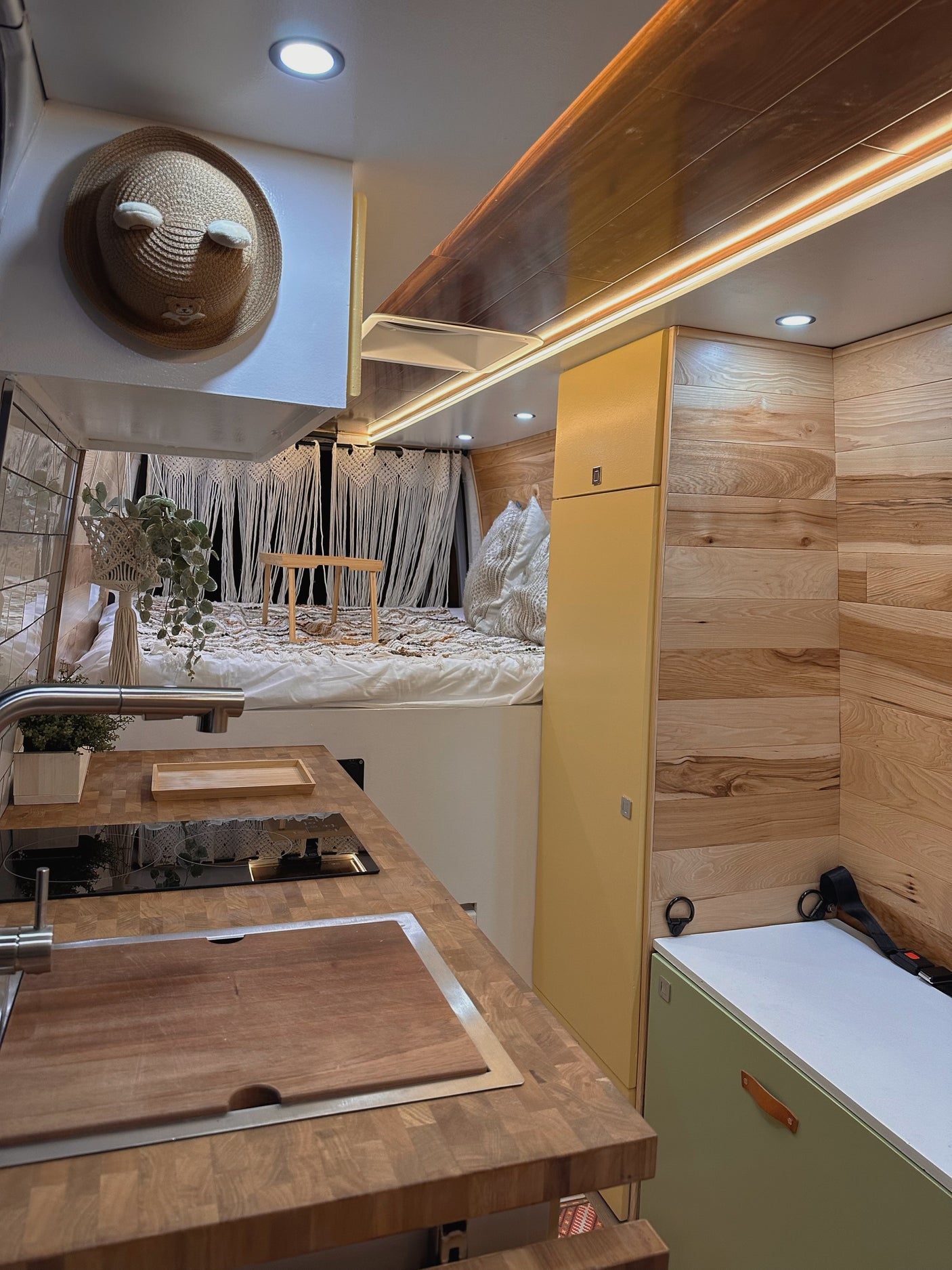 This RV rental interior features a modern kitchen, wooden countertops, cozy bed, and warm wood paneling.