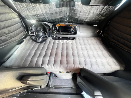 RV rental van with a Luno air mattress laid over front seats & dash, plus window coverings. Ideal for comfortable van camping.