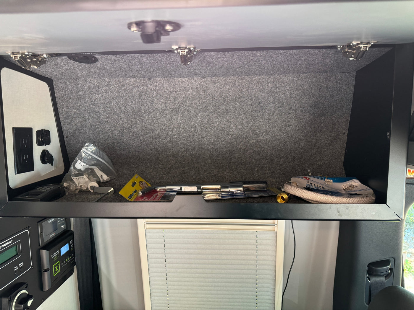 An RV rental's overhead cabinet displaying tools, hoses, and an electrical control panel with a solar charge controller. — photo 19