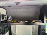 An RV rental's overhead cabinet displaying tools, hoses, and an electrical control panel with a solar charge controller.