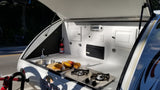 Open rear kitchen of an RV rental teardrop camper, featuring a sink, stove, fruit on counter, and safety equipment.