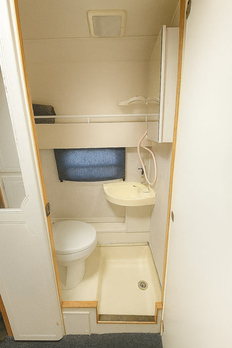 RV rental: Compact onboard bathroom with toilet, small sink/shower combo, and ceiling light. Efficient use of space.
