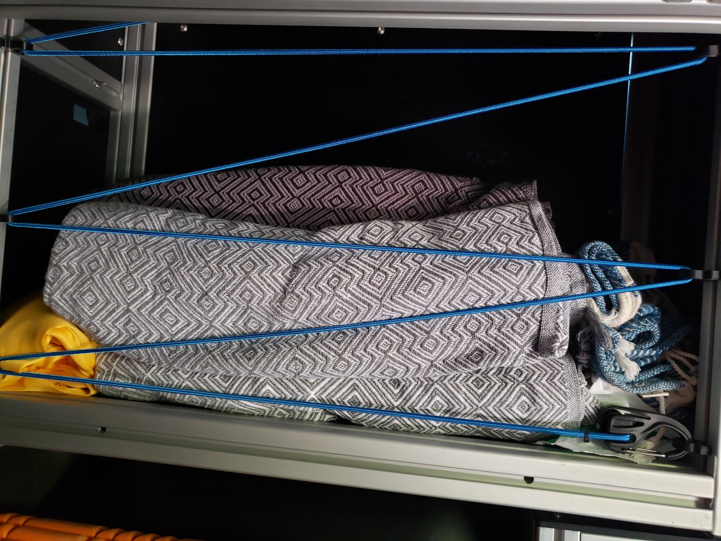 RV rental storage: Patterned blankets neatly secured with blue bungee cords inside a cabinet, preventing items from shifting.