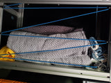 RV rental storage: Patterned blankets neatly secured with blue bungee cords inside a cabinet, preventing items from shifting.