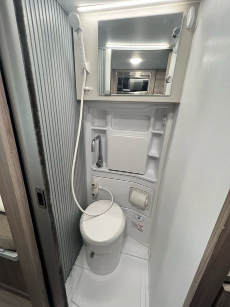 Compact RV rental bathroom showing toilet, shower, sink, and mirror reflecting a microwave.