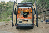 RV rental camper van with open doors, showing its cozy interior, bed, and outdoor setup with an awning and chairs.