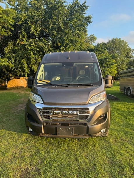 Front view: Dark gray Ram ProMaster camper van for RV rental, parked on grass with trees.