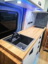 RV rental interior: A bright, modern camper kitchen with a black sink, wood countertops, and blue/hexagonal tiled backsplashes.