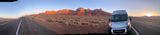 RAM ProMaster RV rental on a desert road, facing majestic red rock cliffs at sunset/sunrise. Perfect for a scenic road trip adventure.