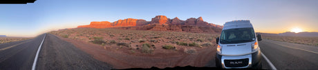 RAM ProMaster RV rental on a desert road, facing majestic red rock cliffs at sunset/sunrise. Perfect for a scenic road trip adventure.