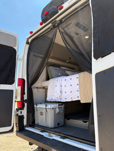 RV rental: Rear view of a camper van's interior, featuring a bed, cooler, and mesh screen, ready for adventure.