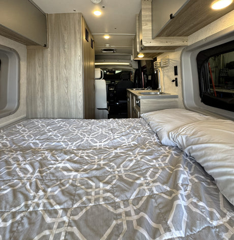 Cozy RV rental interior with a comfy bed, kitchenette, and bright lighting, perfect for your next road trip adventures.