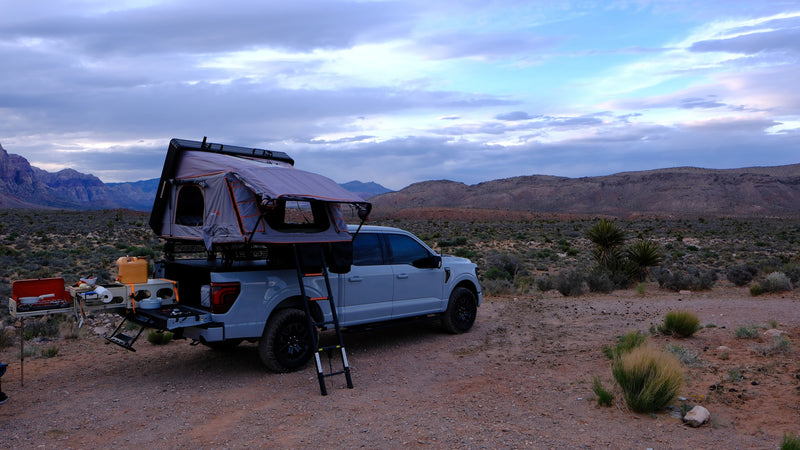 Grey truck with rooftop tent and kitchen setup in a desert landscape. Perfect for an adventurous rv rental trip. — photo 6