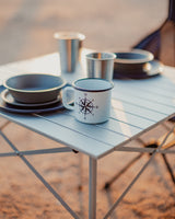 Enjoy outdoor meals with your RV rental. Durable camping dinnerware set, including a compass mug, on a portable table.