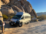 RV rental camper van parked at a desert campsite (#41). Awning extended, surrounded by massive rock formations.