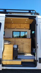 This rv rental camper van features a warm, wood-paneled interior, kitchenette, and fridge, with solar power on the roof.