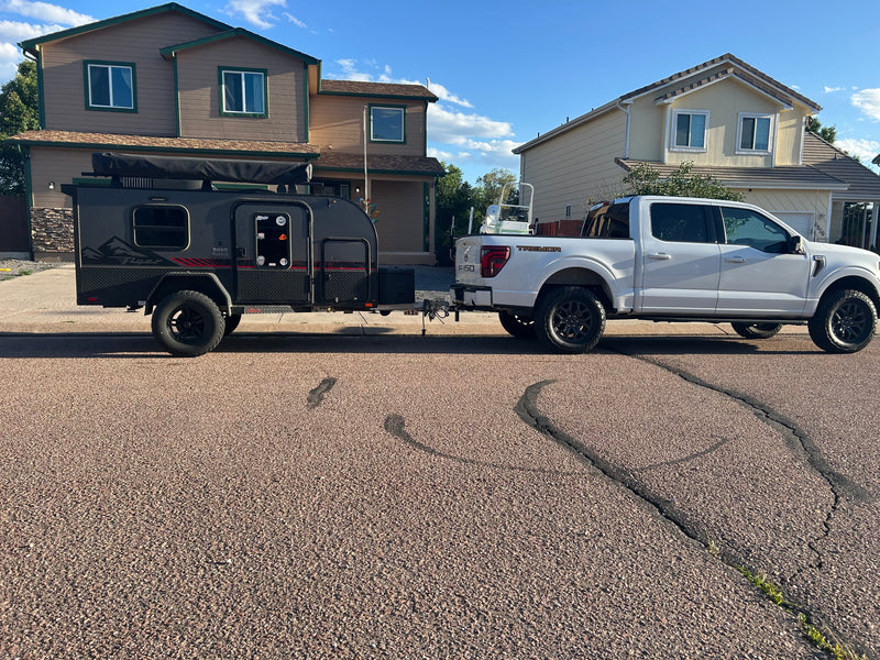 White Ford F-150 Tremor pickup towing a black off-road rv rental trailer, ready for adventure. A boat is in the truck bed. — photo 3