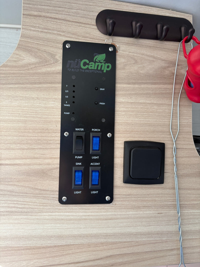 nuCamp RV rental control panel shows tank levels, water pump, and lighting switches. A coat rack is visible above. — photo 10