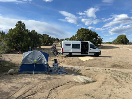 RV rental adventure: People, camper van, tent, and bikes at a scenic desert camp.