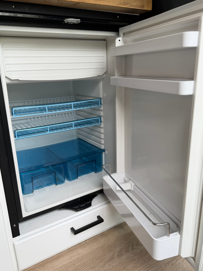 Clean, empty RV rental mini-fridge with open door, showing interior shelves, freezer compartment, and blue storage bins. — photo 12