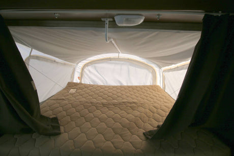 Cozy sleeping area inside an RV rental with a quilted mattress, surrounded by the fabric walls of a pop-up camper.