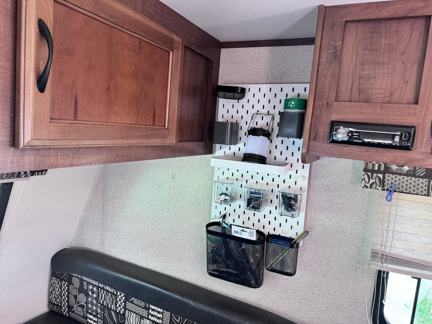 Inside an RV rental: view of organized storage with a white pegboard, wooden cabinets, and a patterned bench seating area. — photo 10