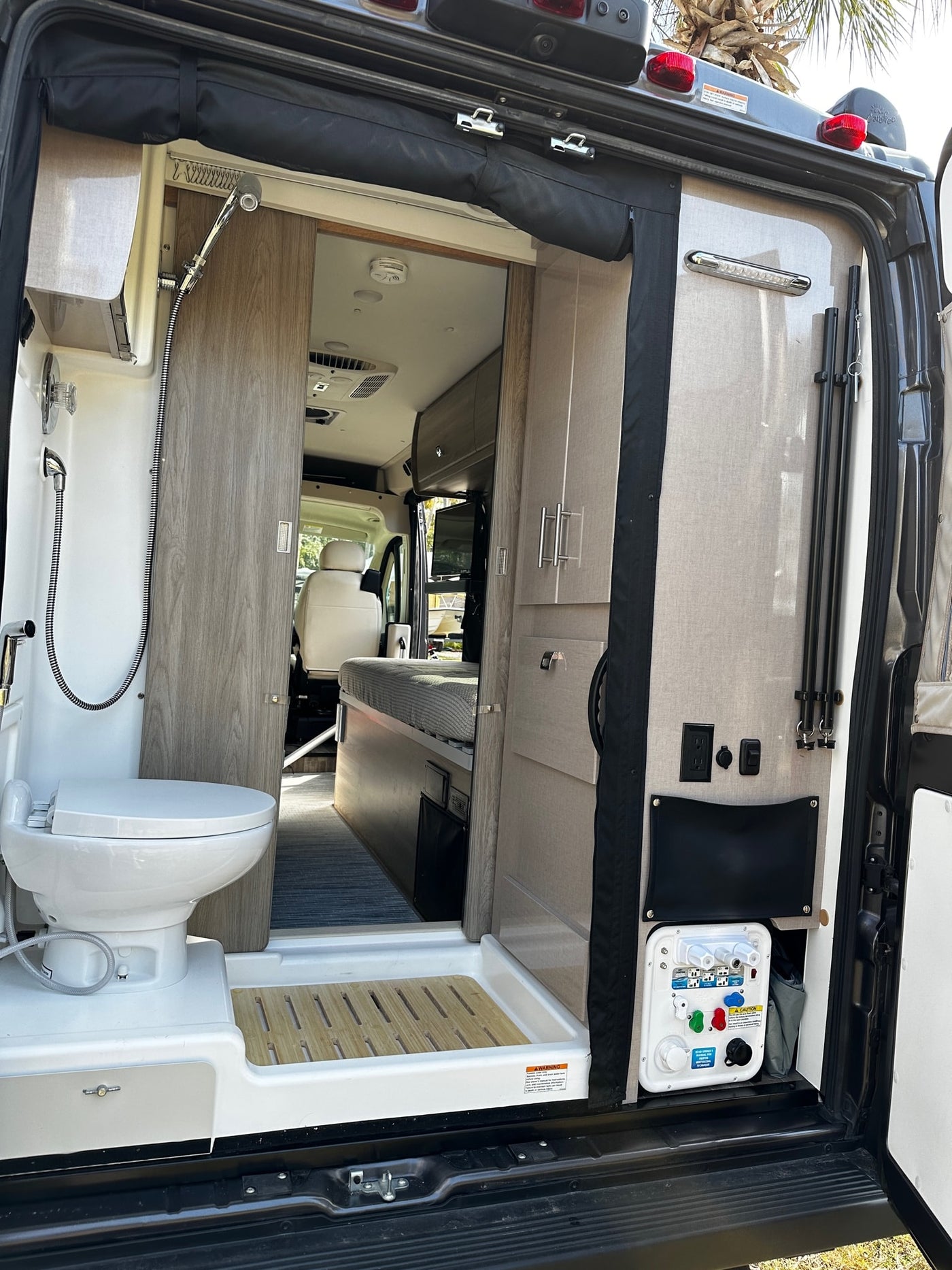 View inside an rv rental from the rear: compact bathroom with shower/toilet, plus utility & power outlets. — photo 17