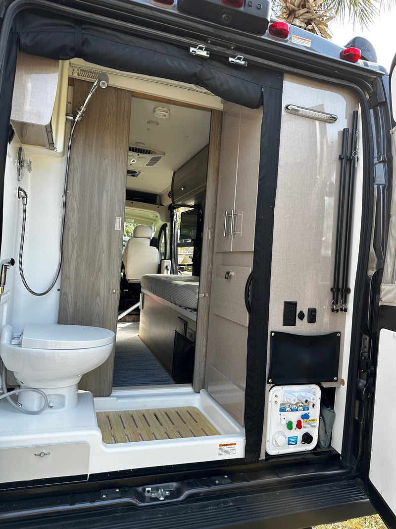 View inside an rv rental from the rear: compact bathroom with shower/toilet, plus utility & power outlets. — photo 17