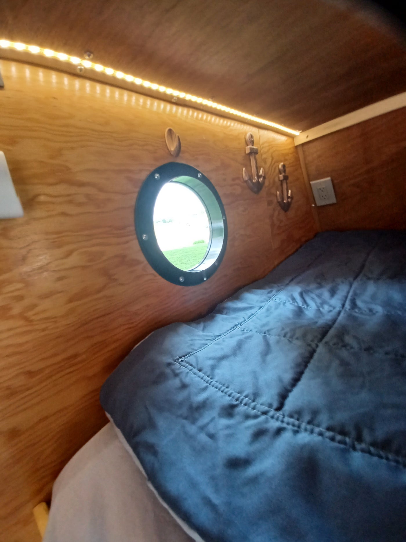 This cozy RV rental interior features warm wooden walls, bright LED lighting, a circular porthole window, anchor decor, and a comfy bed. — photo 18