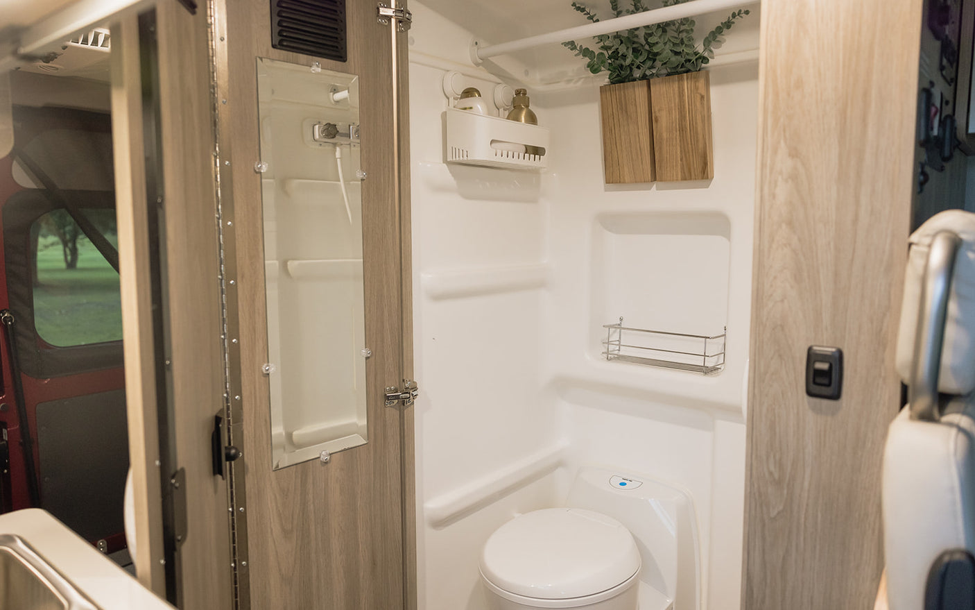 This RV rental boasts a bright, compact bathroom with toilet, shower, storage, and modern wood finishes.