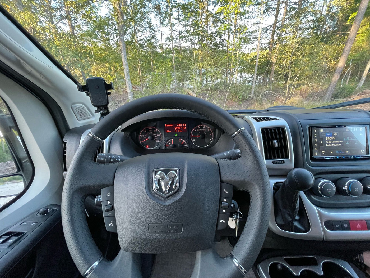 RV rental dashboard view showing the steering wheel, instruments, stereo, and a scenic forest and lake outside. — photo 20