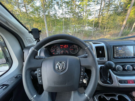 RV rental dashboard view showing the steering wheel, instruments, stereo, and a scenic forest and lake outside.