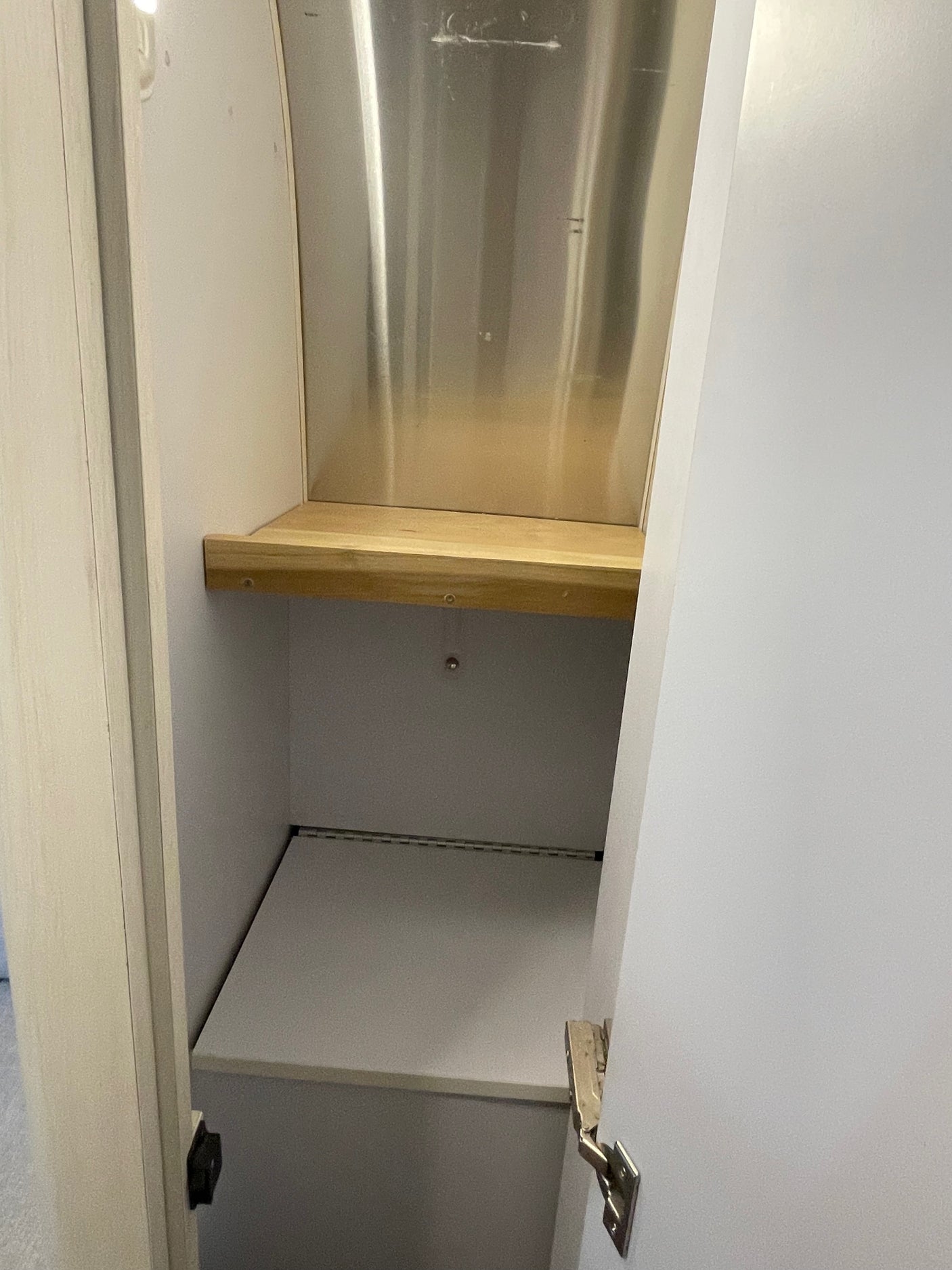 Efficient RV rental cabinet: Features a wooden shelf, polished metal back, and lower hinged storage. Optimized for compact living.