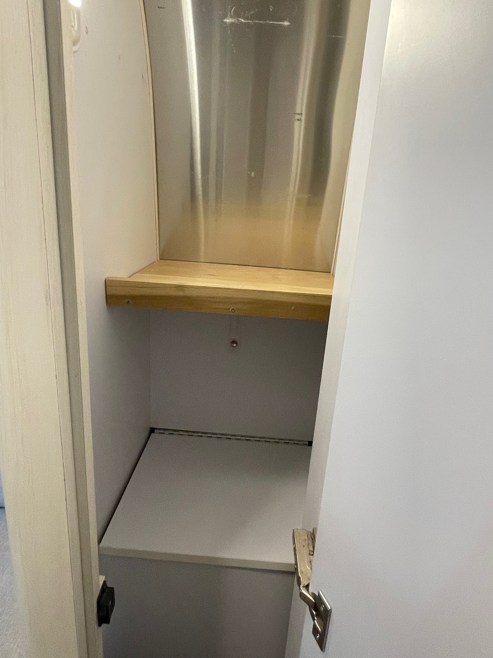 Efficient RV rental cabinet: Features a wooden shelf, polished metal back, and lower hinged storage. Optimized for compact living.