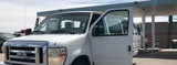White Ford van for RV rental, driver's door open, parked under a canopy with other rental vehicles.